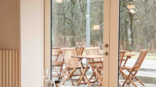 Un comedor con mesas y sillas de madera, una pared divisoria de vidrio y vistas al exterior.