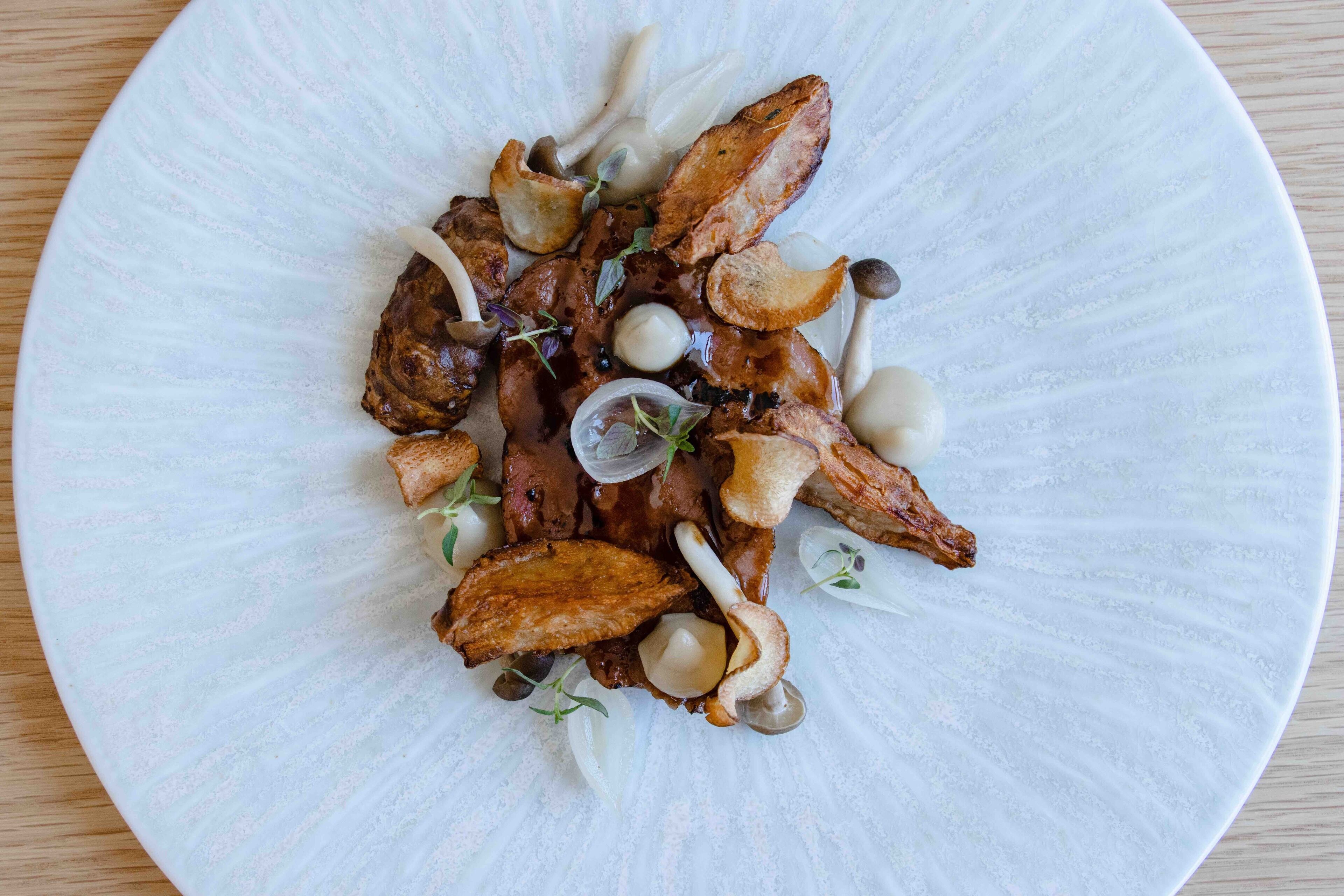 A white plate with food items including meat, mushrooms, and garnishes.
