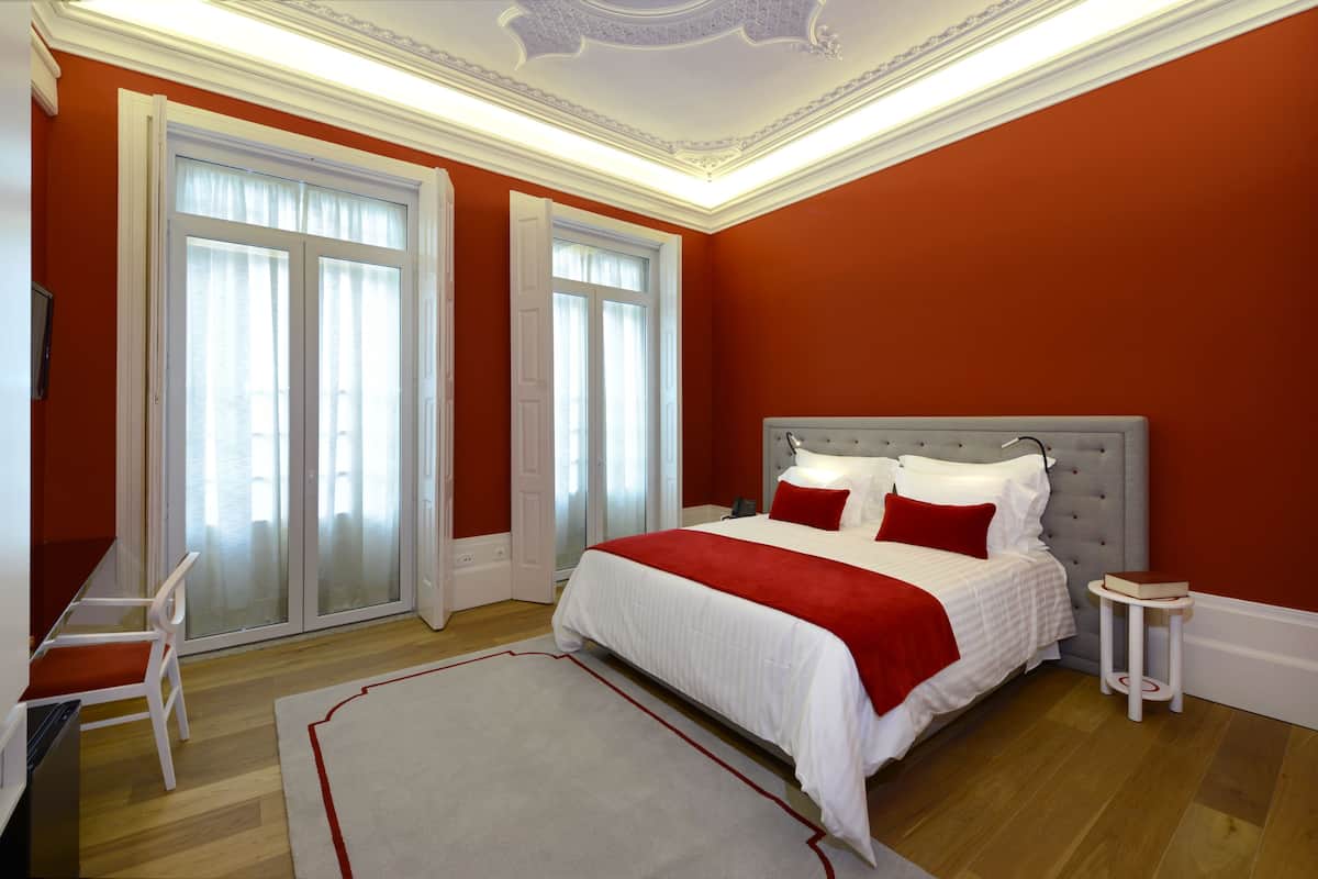 Een slaapkamer met een groot bed, witte beddengoed, rode accenten en een houten vloer.