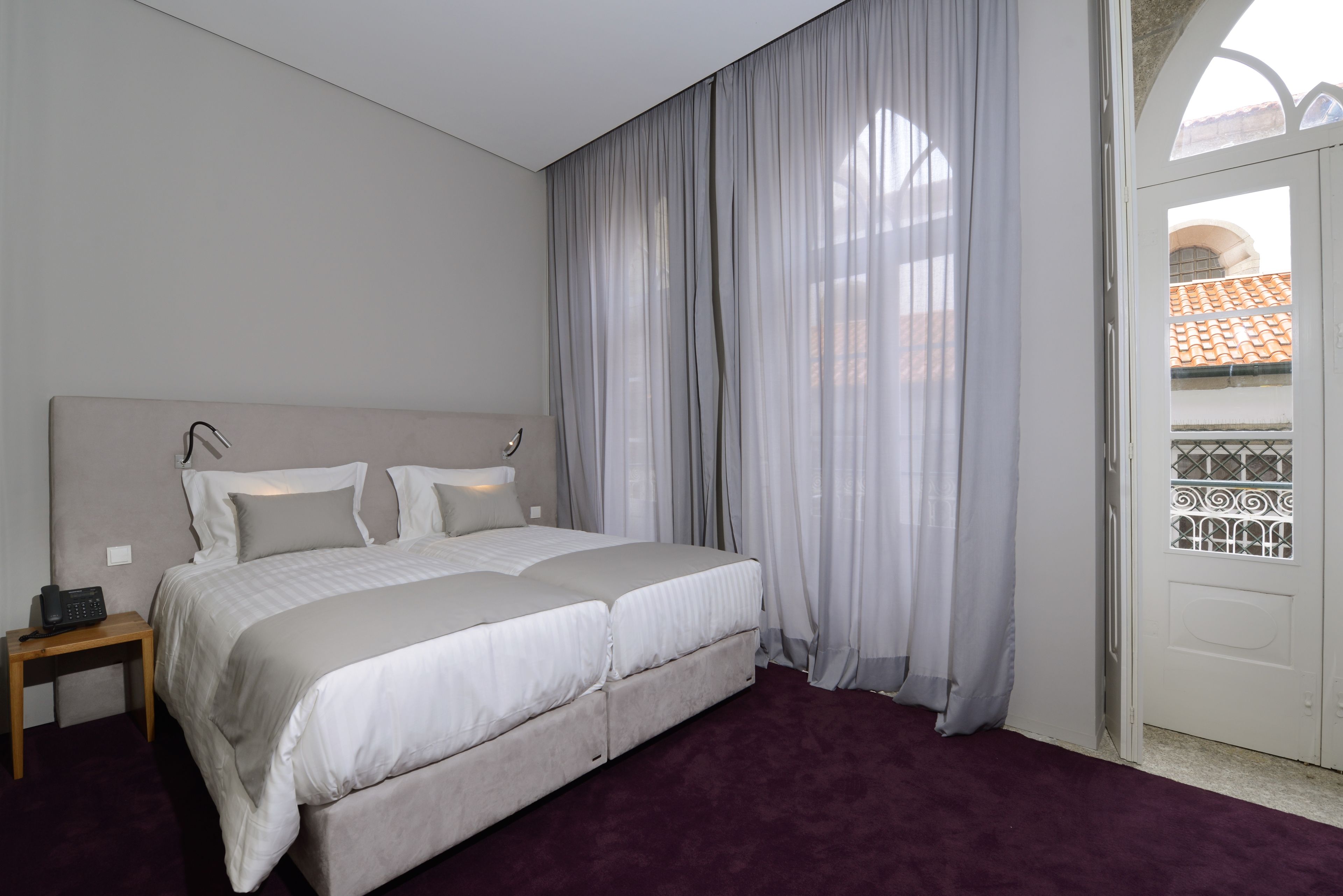 A bedroom with a large bed, a bedside table, and a window with sheer curtains.