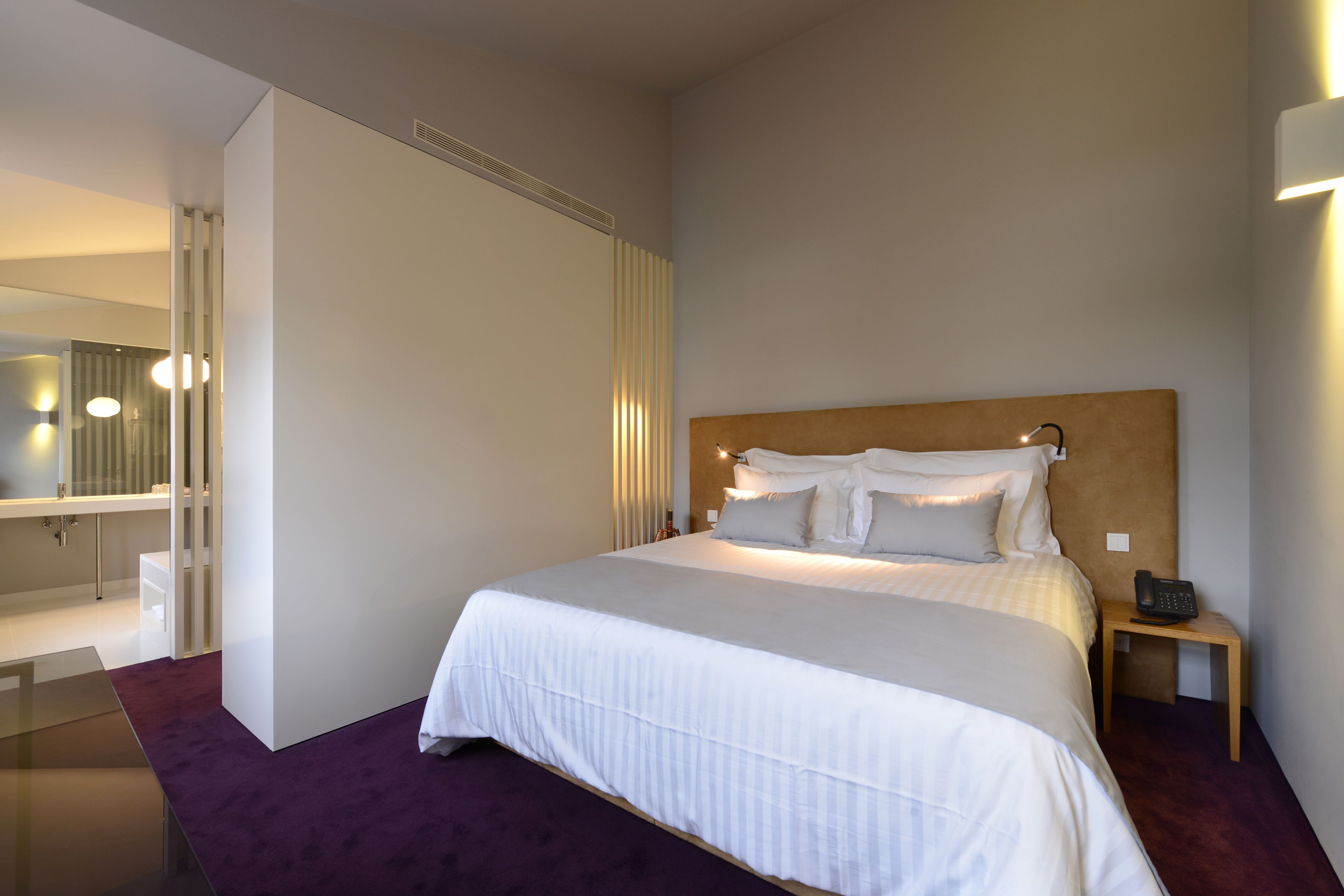 A modern hotel room with a large bed, a bedside table with a phone, and a mirror.