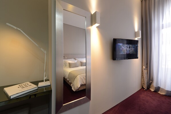 A hotel room with a bed, a bedside table with a lamp, a TV mounted on the wall, and a window with curtains.
