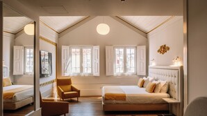 Ein Schlafzimmer mit einem großen Bett, einem Sessel, einem Spiegel und einem Fenster mit Blick auf Gebäude.