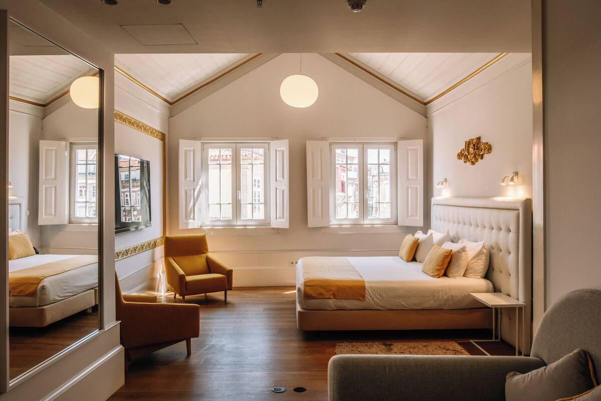 Een slaapkamer met een groot bed, een stoel, een spiegel en een raam met uitzicht op gebouwen.