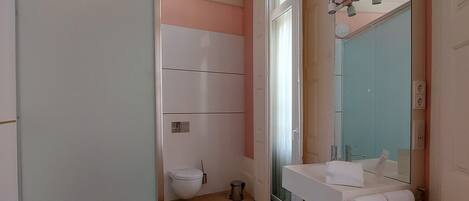 A bathroom with a white sink, a mirror, and a toilet. There is a towel rack and a trash can.