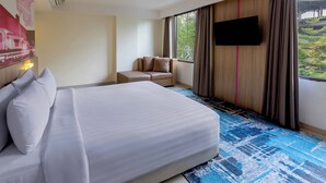 A hotel room with a large bed, a sofa, a TV mounted on the wall, and a window with curtains. - favehotel Hyper Square (Bandung)