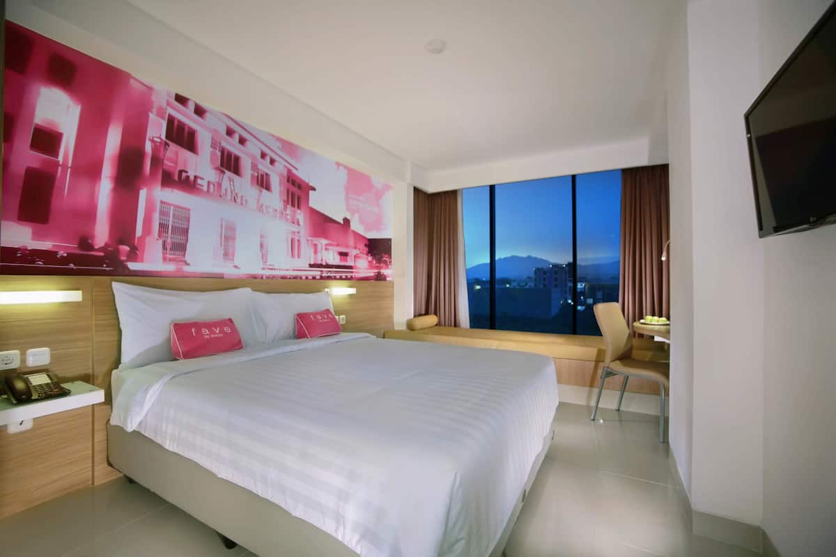 A hotel room with a large bed, a desk with a phone, a chair, a TV, and a large window with a city view.