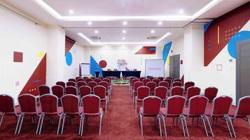 Une salle de conférence avec des rangées de chaises rouges, une scène avec un pupitre et une pancarte « TRAVAIL D’ÉQUIPE » accrochée au mur.