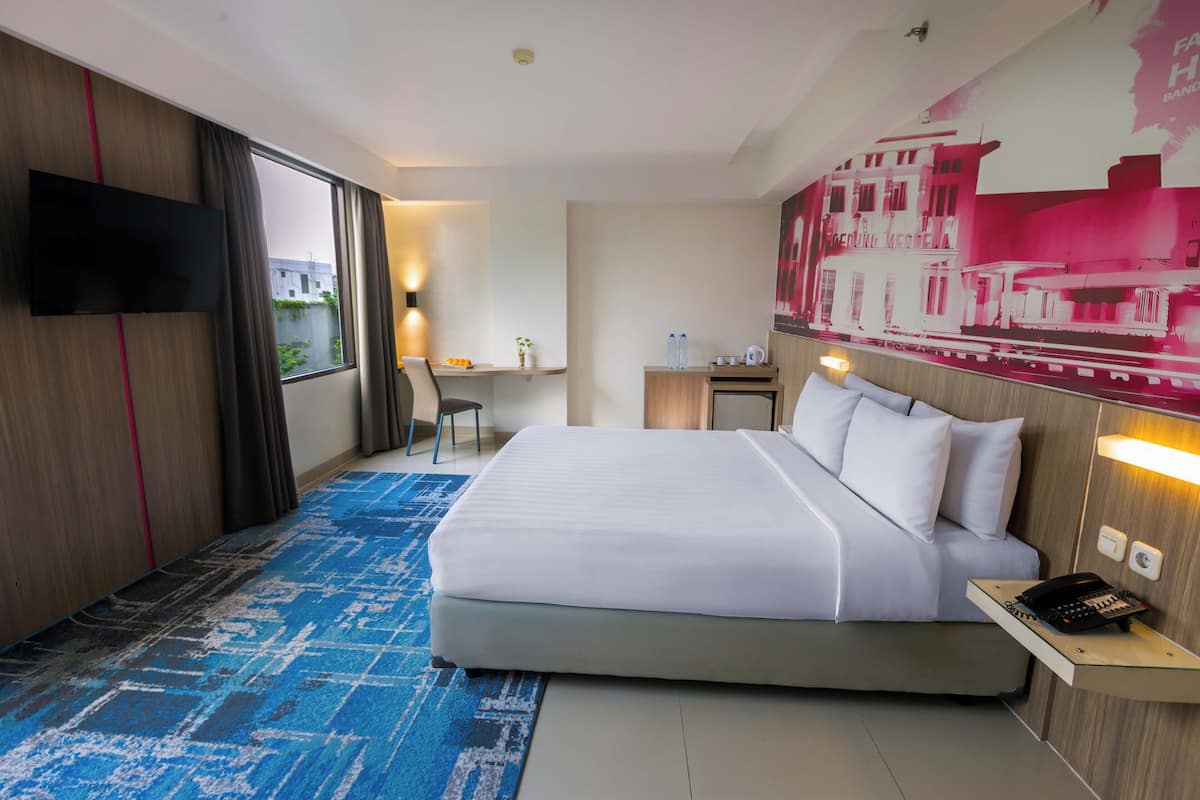 A hotel room with a large bed, a desk, a chair, a TV, and a painting on the wall.