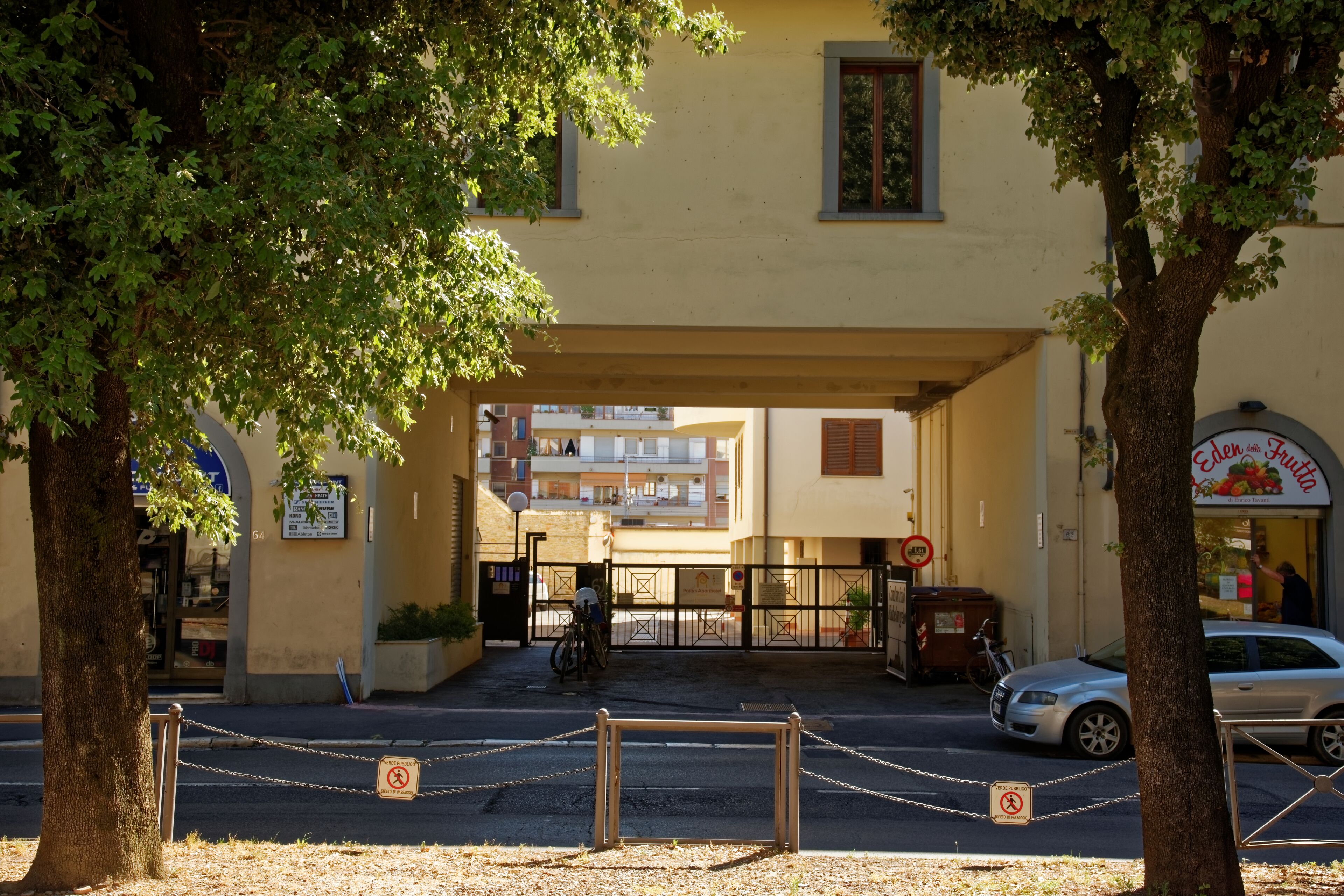 A building entrance with a gated driveway, a bicycle parked inside, and a car parked outside.