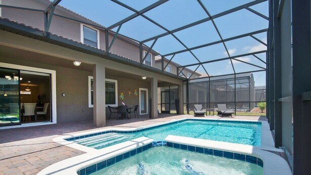 Un área de piscina exterior techada con un jacuzzi, asientos en terraza y una estructura de vidrio.