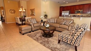 Una sala de estar con un sofá modular, un sillón estampado, una mesa de centro y un comedor con sillas.