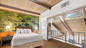 A bedroom with a bed, nightstand, and a mural of a forest. There is a balcony with a wooden railing and a view of the outside. - Northern Queen Inn (Nevada City)