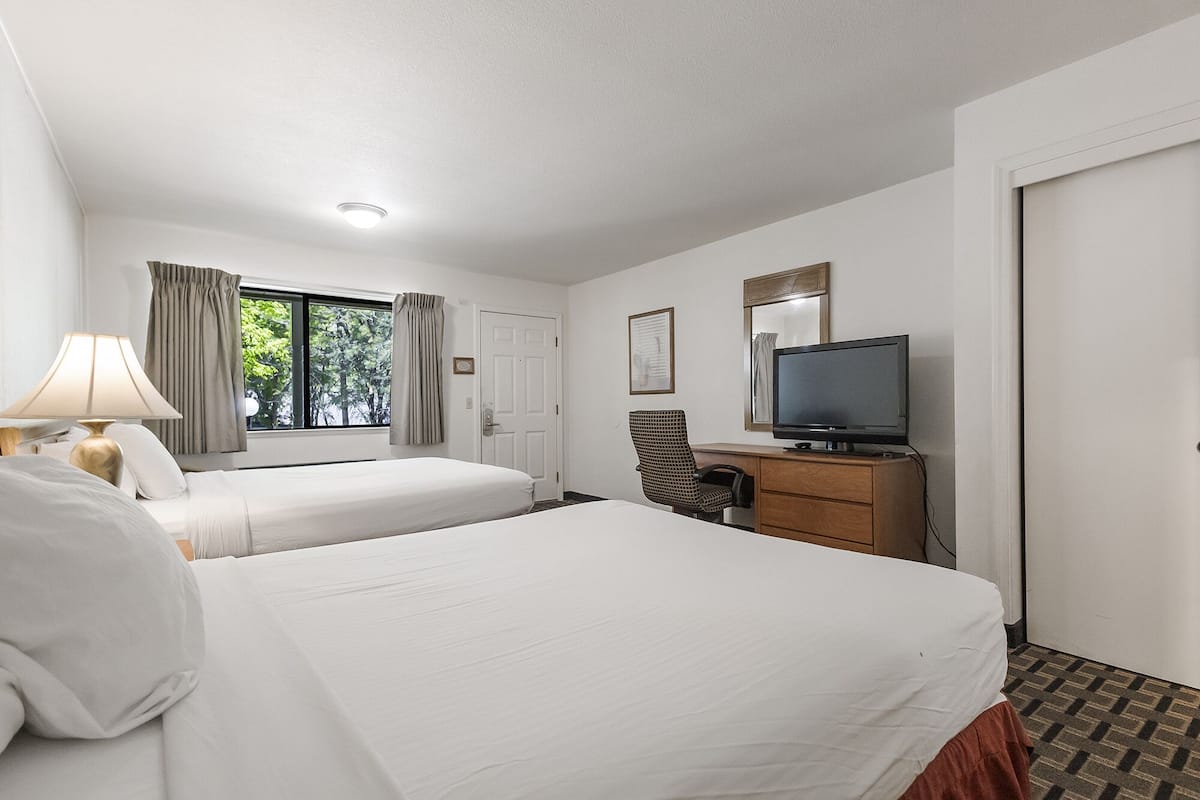 A hotel room with two beds, a television, a desk, and a window with curtains.