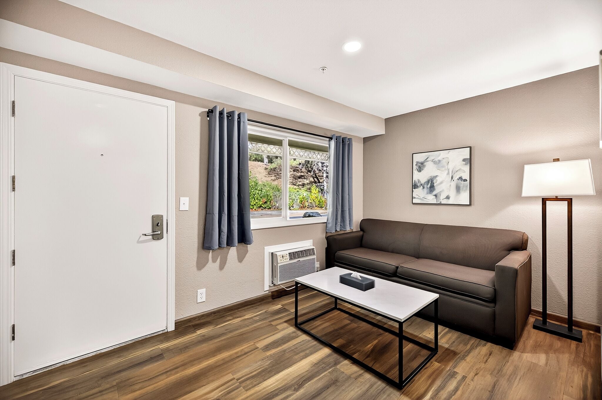 Un salon moderne avec un canapé marron, une table basse blanche, un lampadaire et une fenêtre avec des rideaux.