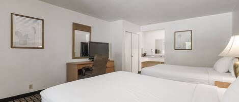 A hotel room with two beds, a desk with a computer, a TV, and a mirror.