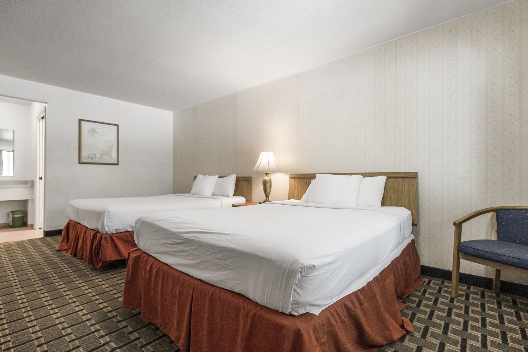A hotel room with two beds, a chair, and a lamp.