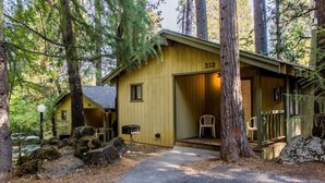 A rustic cabin with a number 312 sign, surrounded by tall trees and a gravel path. - Northern Queen Inn (Nevada City)