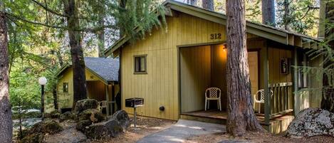 A rustic cabin with a number 312 sign, surrounded by tall trees and a gravel path.