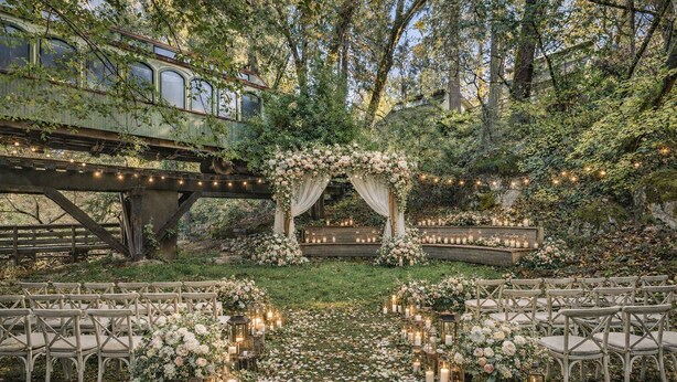 An outdoor wedding venue with a rustic arch decorated with flowers, a wooden bridge, and string lights. - Northern Queen Inn (Nevada City)