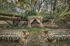 An outdoor wedding venue with a rustic arch decorated with flowers, a wooden bridge, and string lights. - Northern Queen Inn (Nevada City)