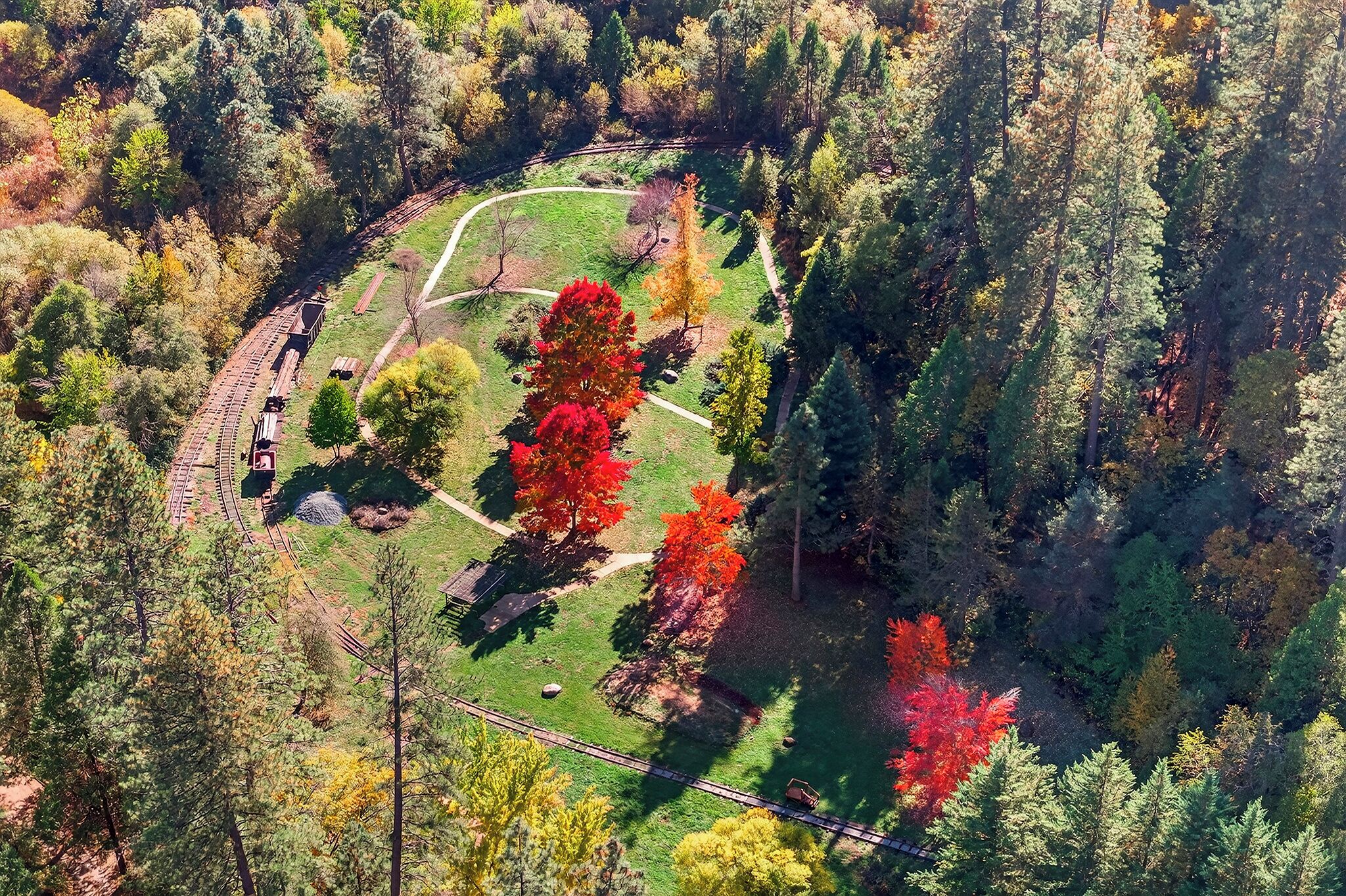 An aerial view of a park with a winding path, a small building, and a train track.