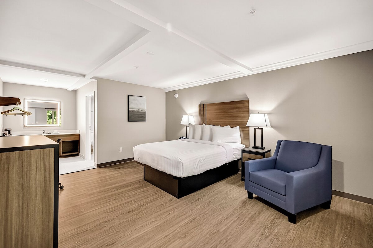 A hotel room with a bed, bedside tables, a chair, a desk, and a mirror.