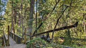 A wooden bridge in a forested area with a metal structure in the background. - Northern Queen Inn (Nevada City)