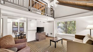 A spacious living area with a high ceiling, a balcony, a flat-screen TV, and a dining area with a table and chairs. - Northern Queen Inn (Nevada City)