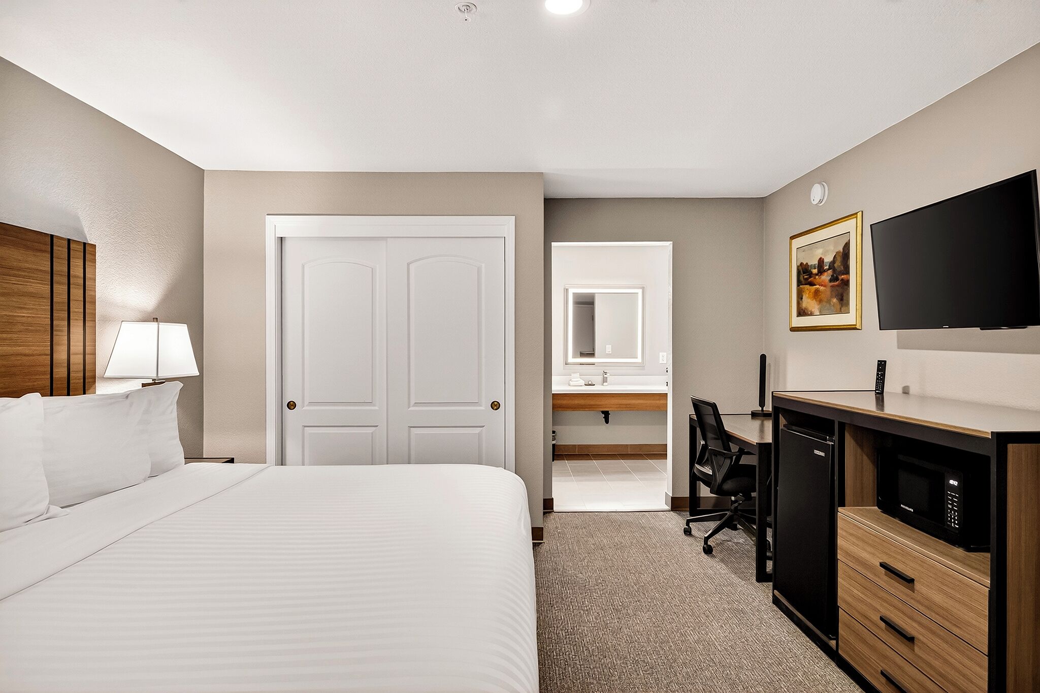 A hotel room with a bed, desk, refrigerator, microwave, and a TV.