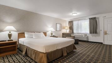 Een hotelkamer met een groot bed, twee nachtkastjes met lampen, een stoel, een airconditioningapparaat en een deur.