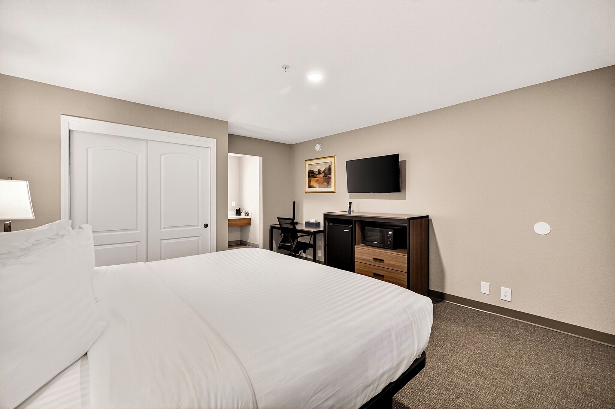 A hotel room with a large bed, a desk with a chair, a television, and a microwave.