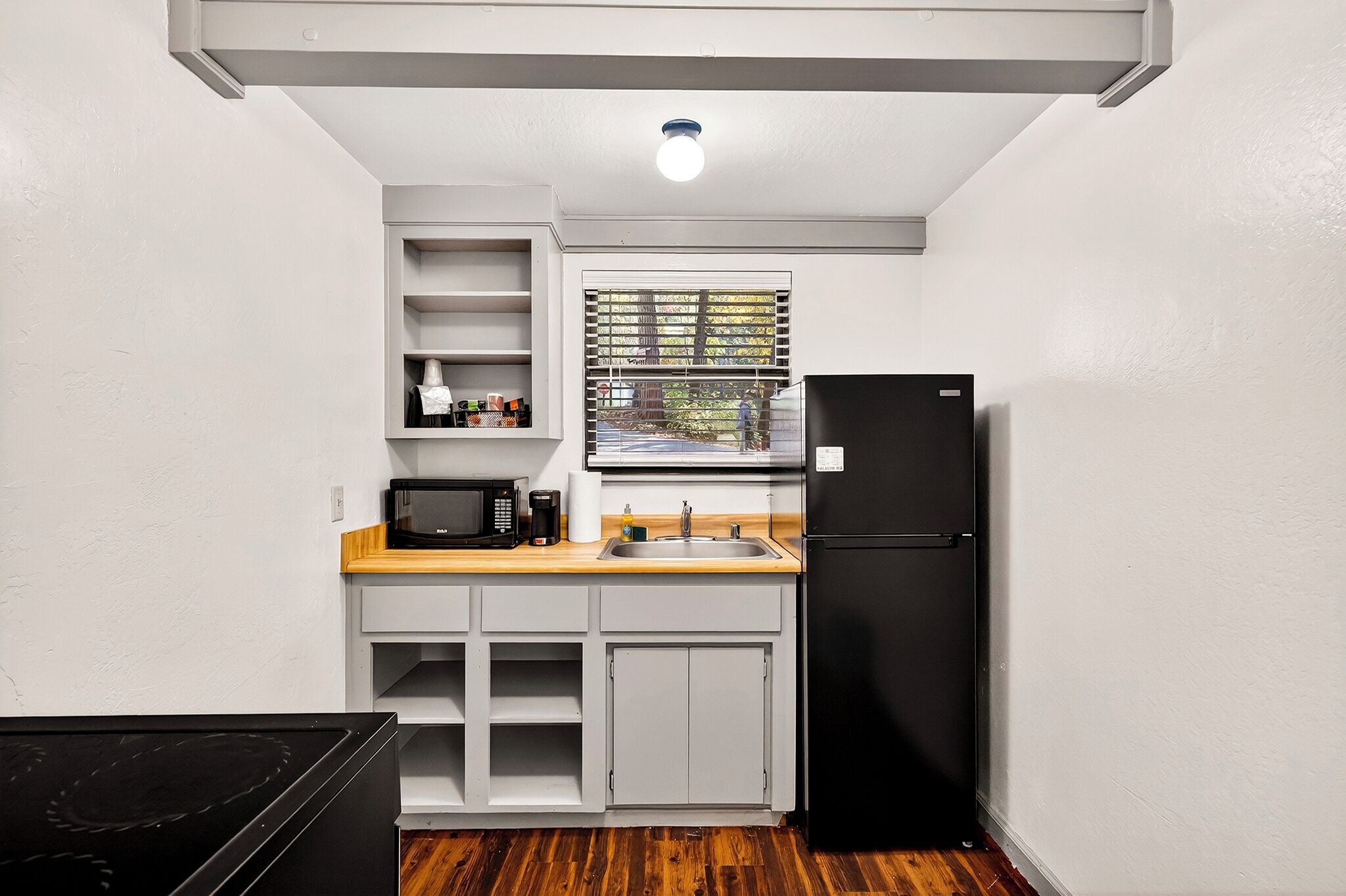 Cocina compacta con armarios blancos, refrigerador negro, microondas y encimera de madera.