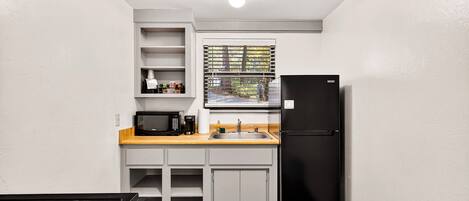 Cocina compacta con armarios blancos, refrigerador negro, microondas y encimera de madera.