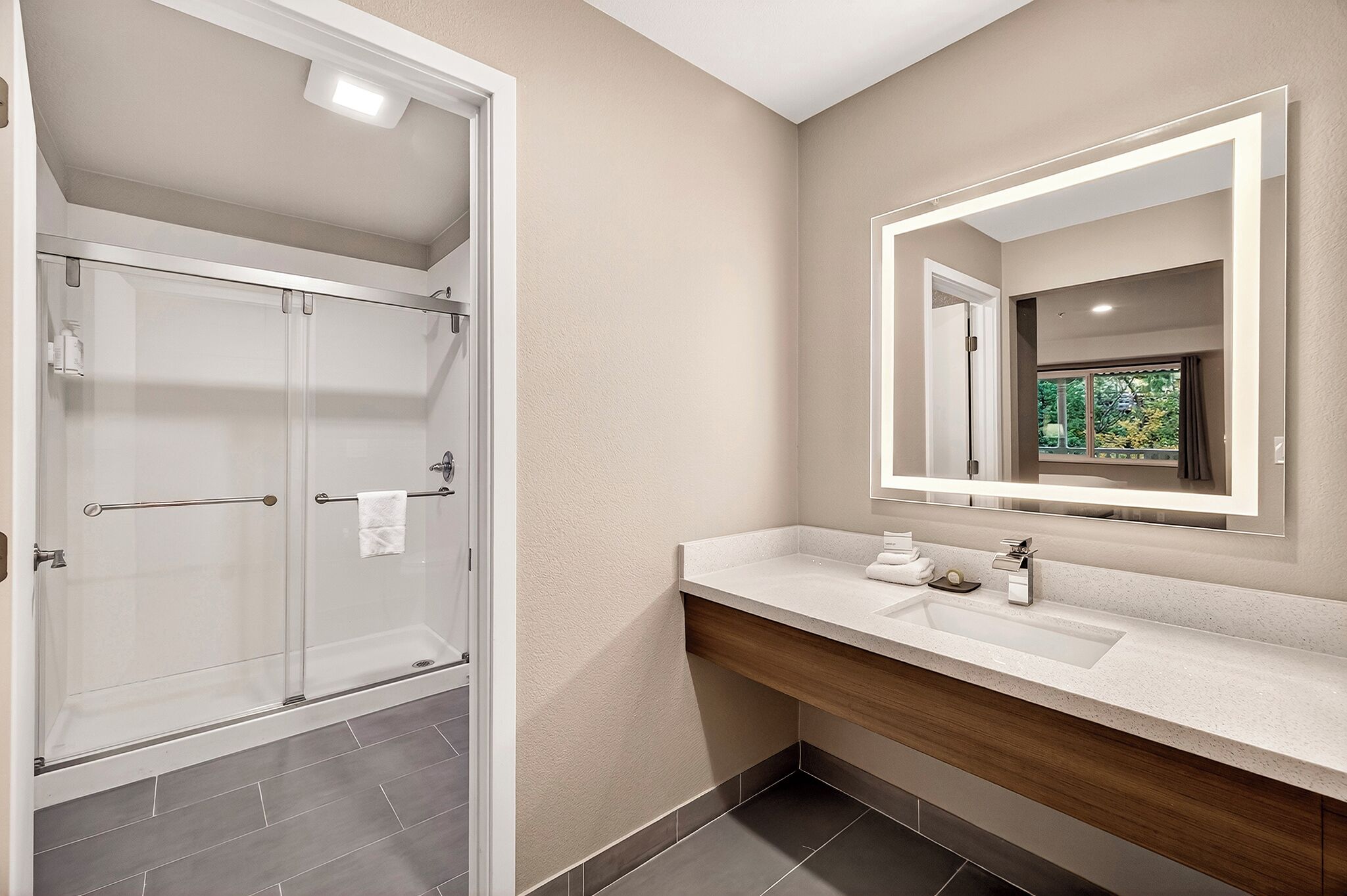 A modern bathroom with a glass-enclosed shower, a large mirror, and a wooden vanity.