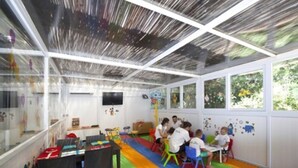 Une salle de classe où des enfants sont assis à des tables, avec des tapis colorés sur le sol et des affiches éducatives accrochées aux murs.