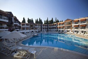 A swimming pool surrounded by lounge chairs and umbrellas, with multi-story buildings in the background.