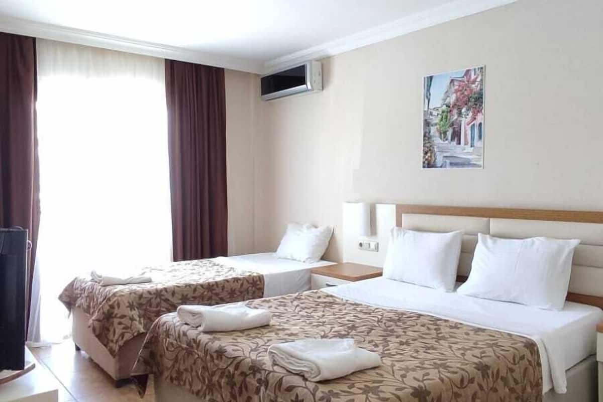 Una habitación de hotel con dos camas, una silla, un escritorio, un cuadro y una ventana con cortinas.