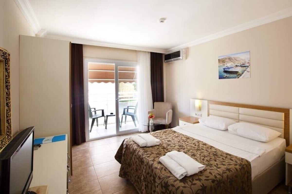 Habitación de hotel con cama, escritorio, silla, televisor y balcón con sillas.