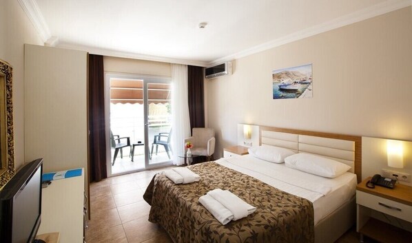 A hotel room with a bed, a desk, a chair, a TV, and a balcony with chairs.