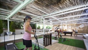 Un espace de remise en forme extérieur abrité, équipé de matériel d'exercice, d'un tapis de course et d'un sol en gazon synthétique vert.