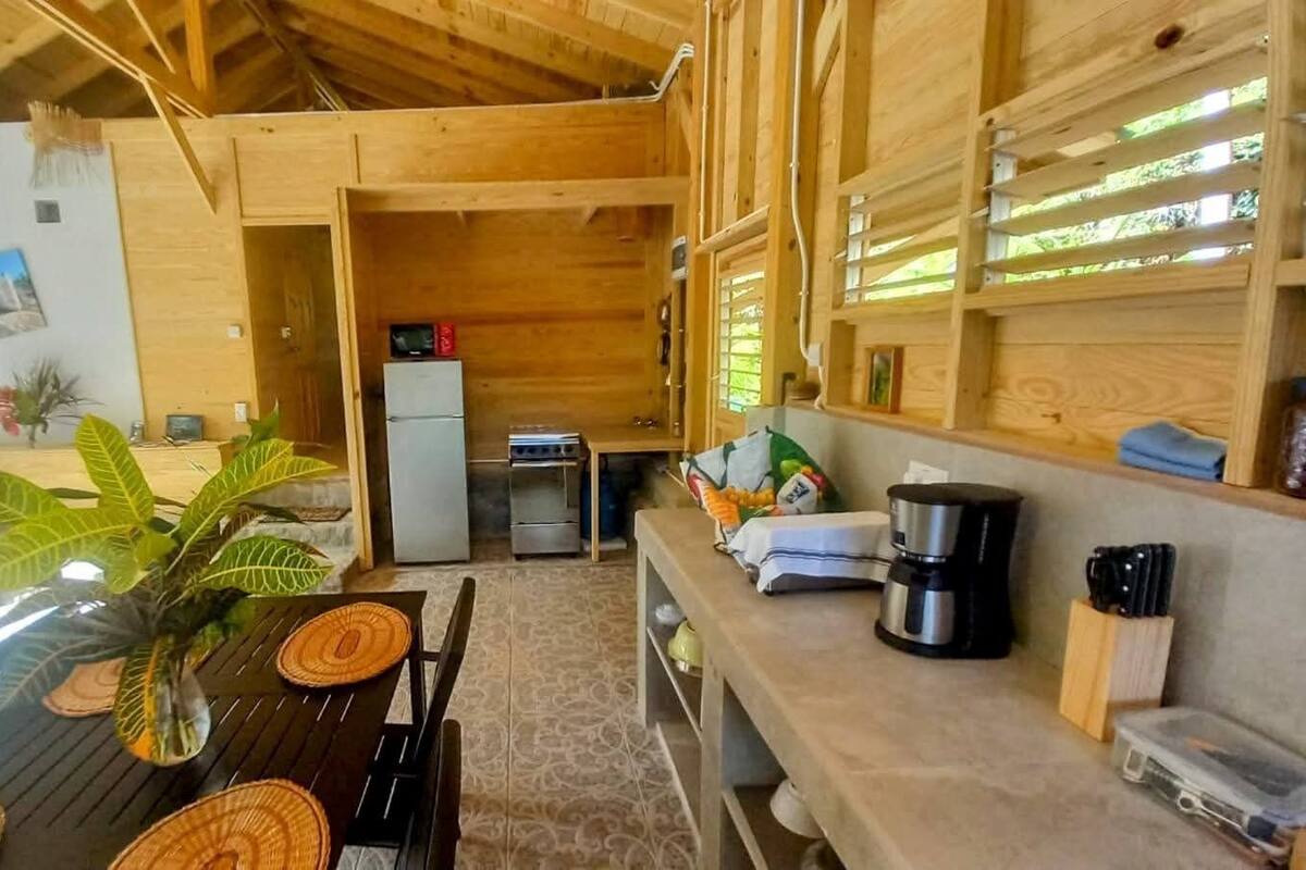 Een houten interieur met een eettafel, stoelen, een koffiezetapparaat en een koelkast.