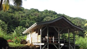 A wooden structure with a covered porch, surrounded by lush greenery and a stone wall.