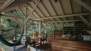 A covered outdoor seating area with wicker furniture, a wooden table, and a hammock.