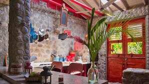 A stone-walled dining area with a red door, a table with chairs, and a hanging light fixture.