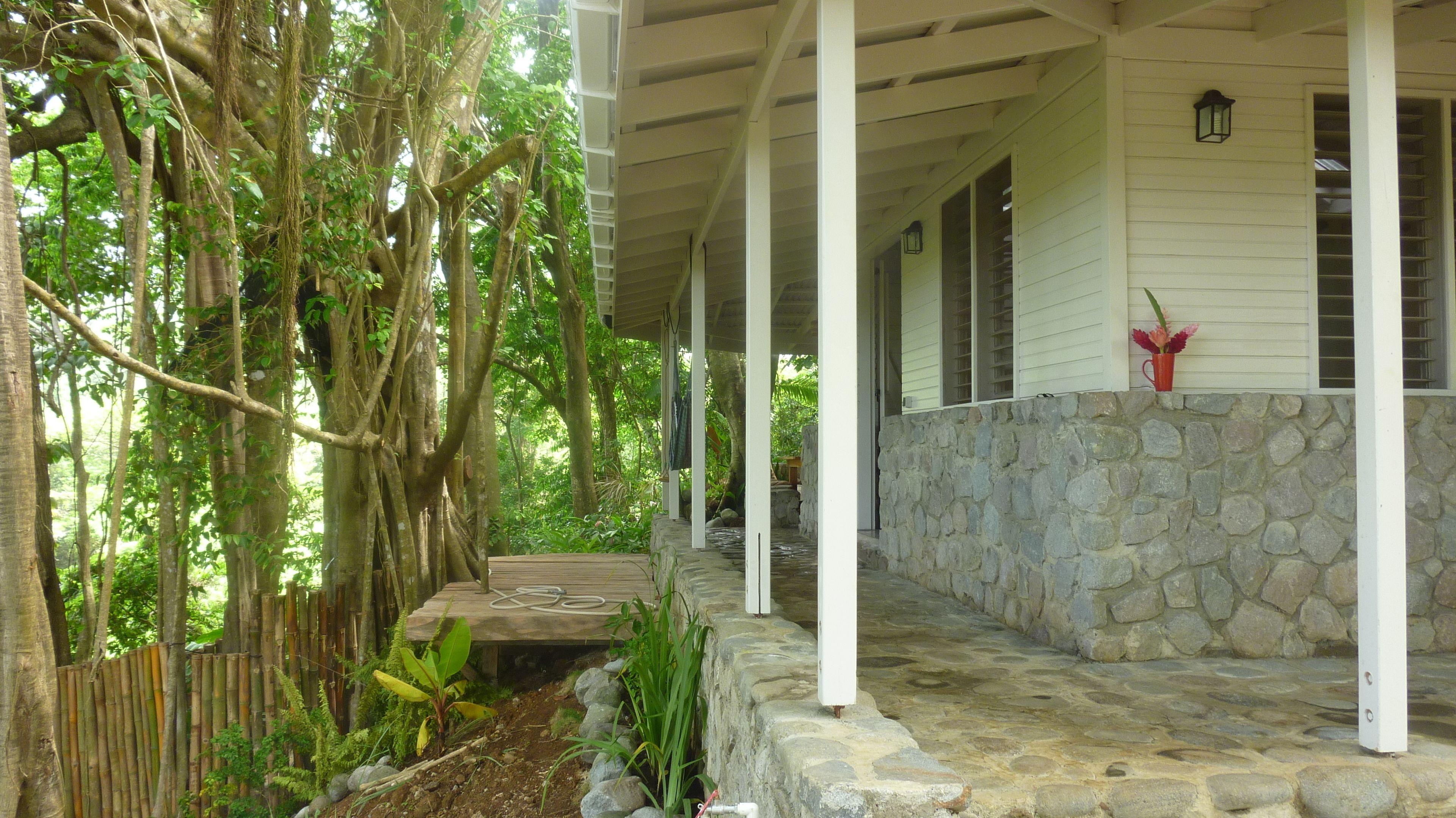 A covered porch with stone walls and a wooden deck, surrounded by lush greenery and trees.