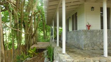 A covered porch with stone walls and a wooden deck, surrounded by lush greenery and trees.