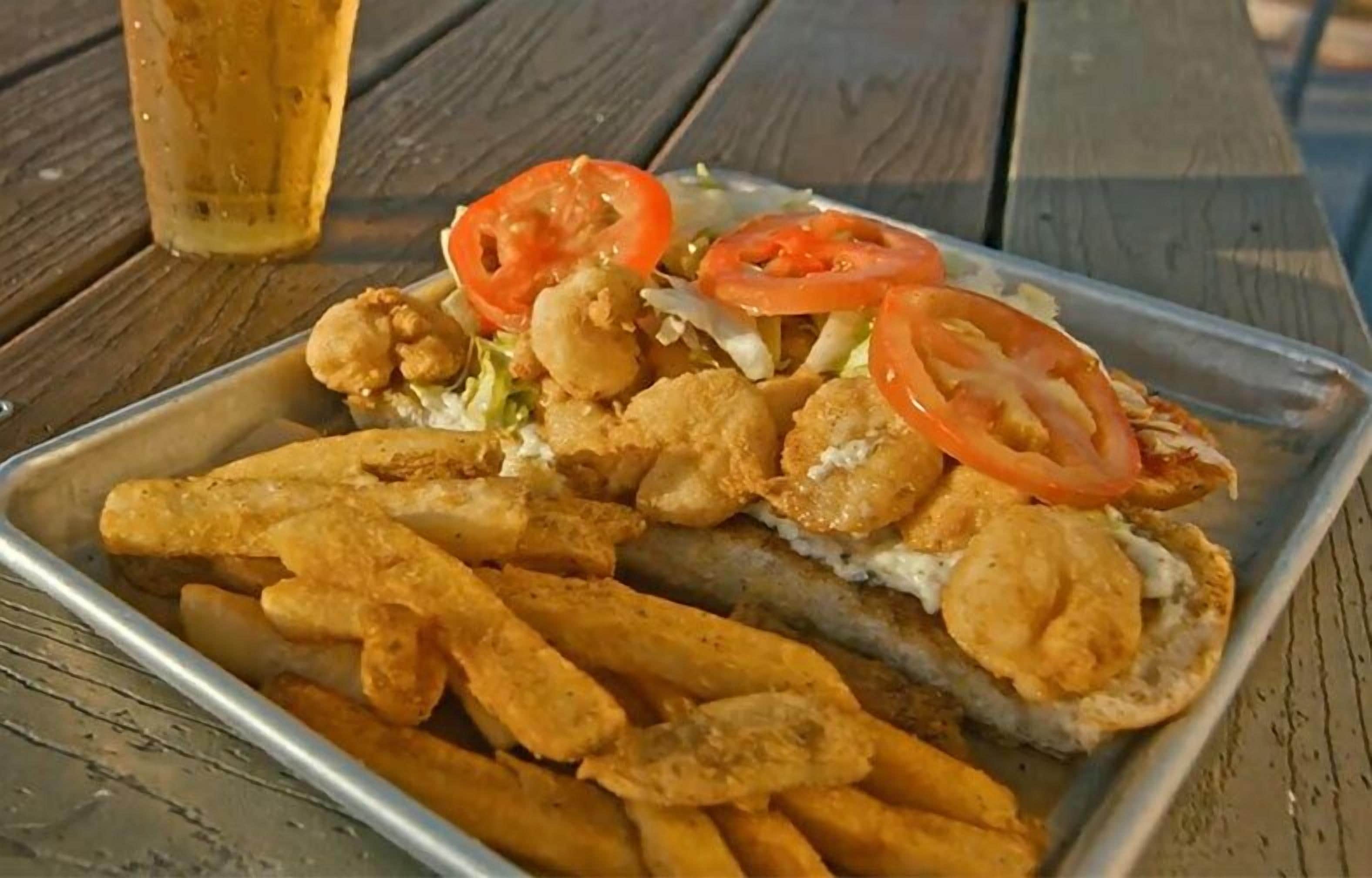 A tray with fried seafood, including shrimp and fish, accompanied by fries and sliced tomatoes, on a wooden table.