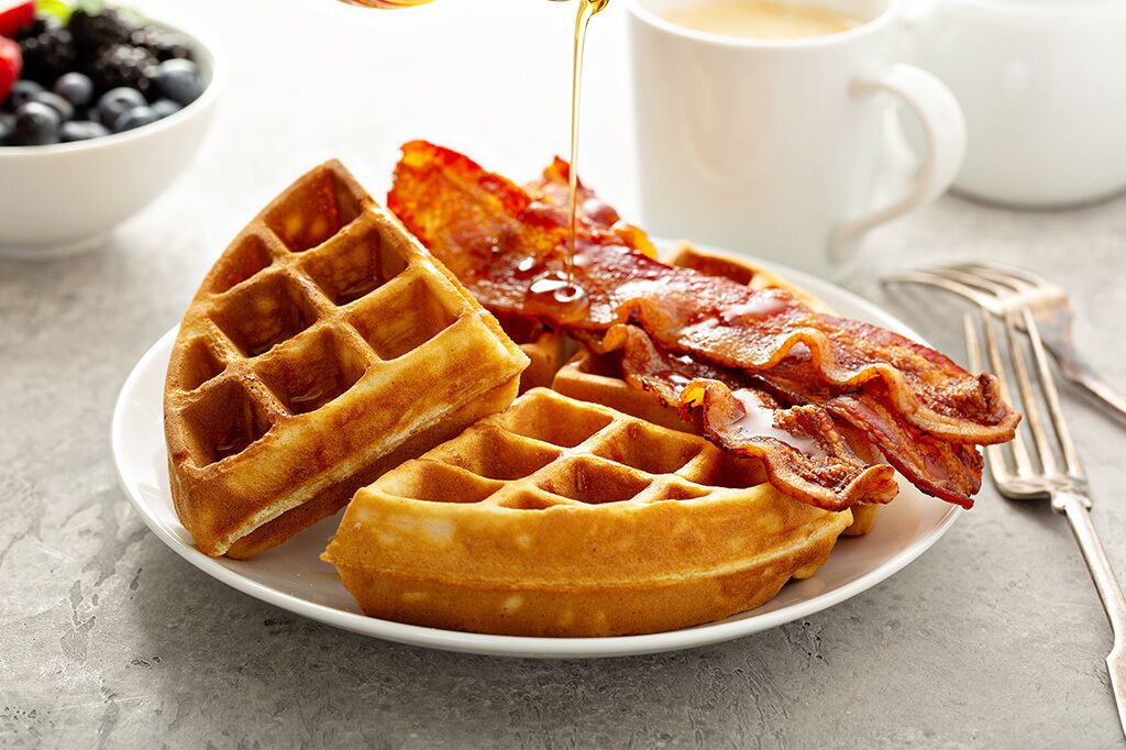 Une assiette avec deux gaufres, du bacon et du sirop.