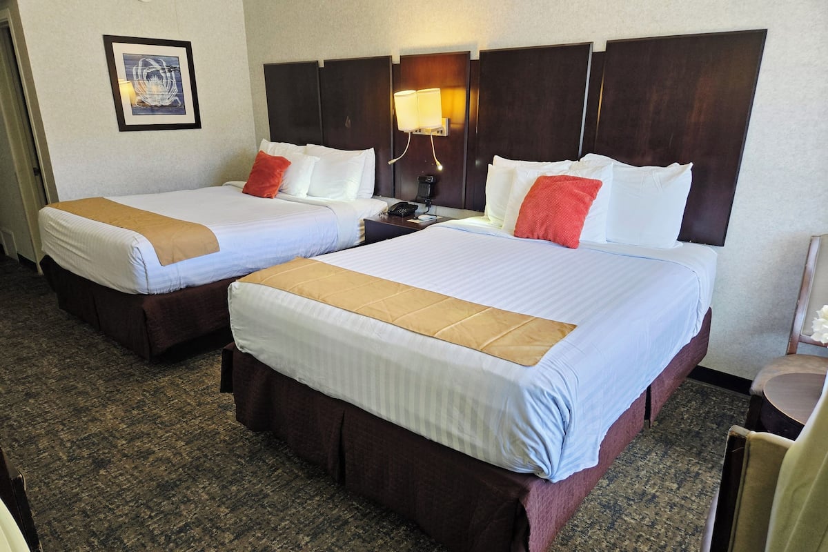 Two double beds with headboards, a bedside table with a lamp, and a framed picture on the wall.